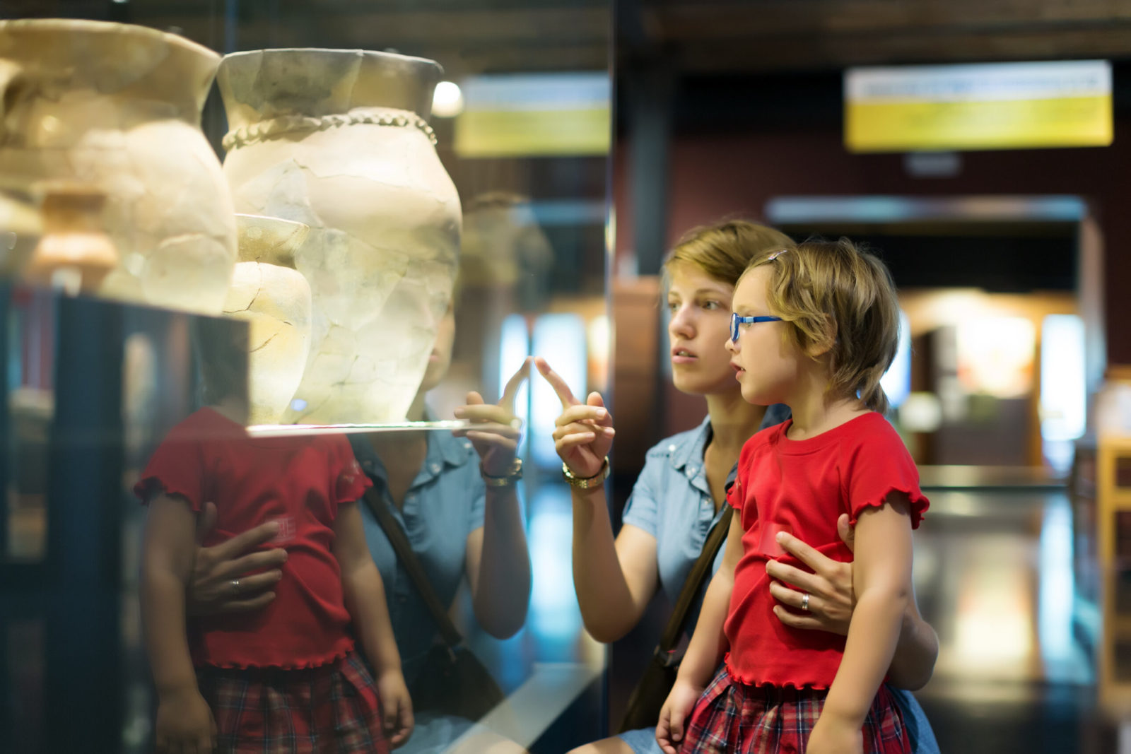 An adult and a young girl are looking at a large vase in a museum