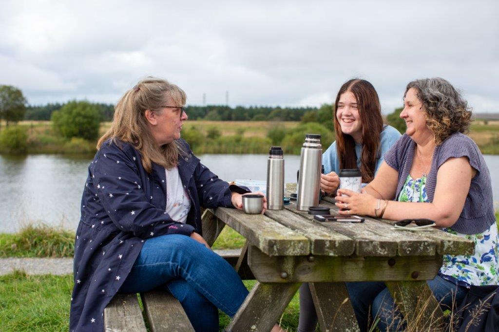 Three ladies enjoying tea on a park bench