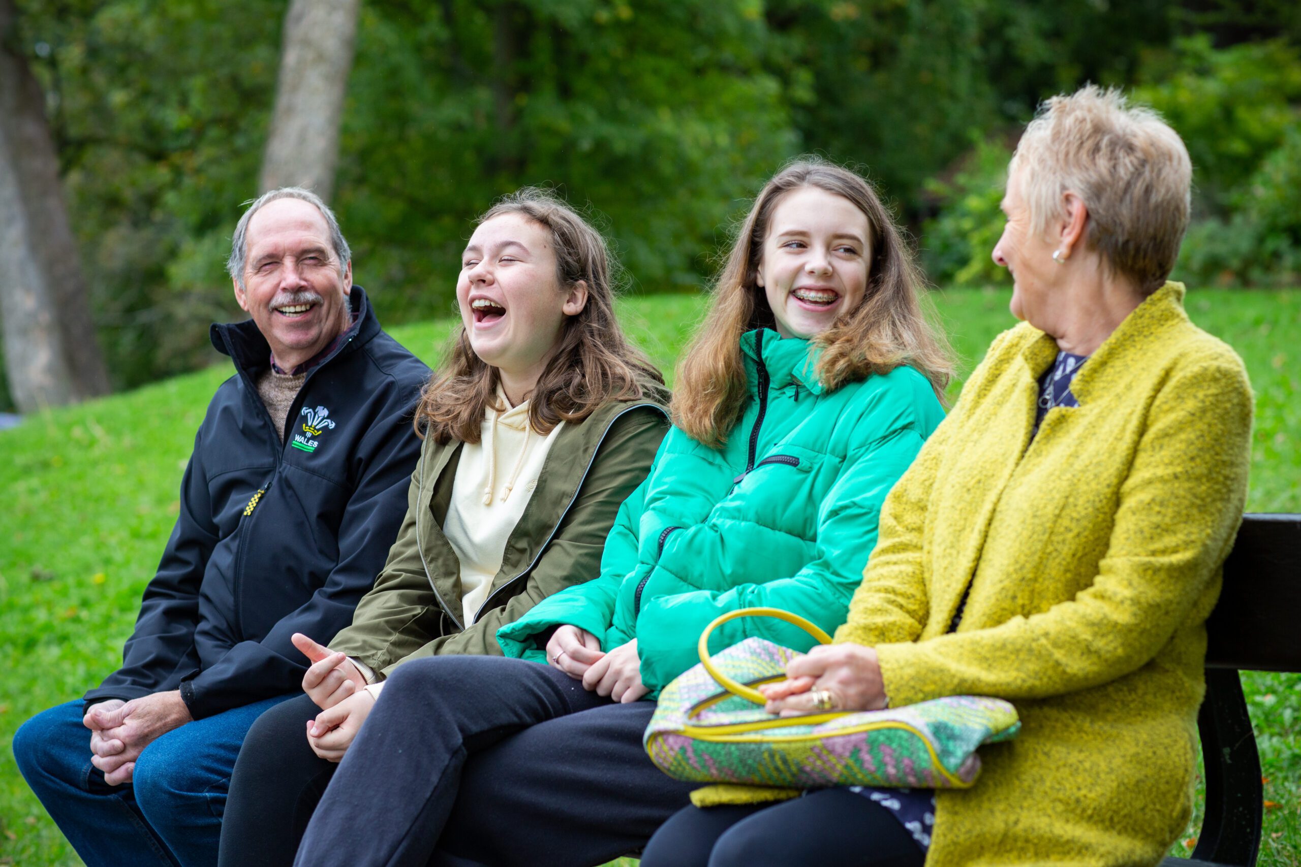 Two teenage girls laughing with a couple sitting on a park bench