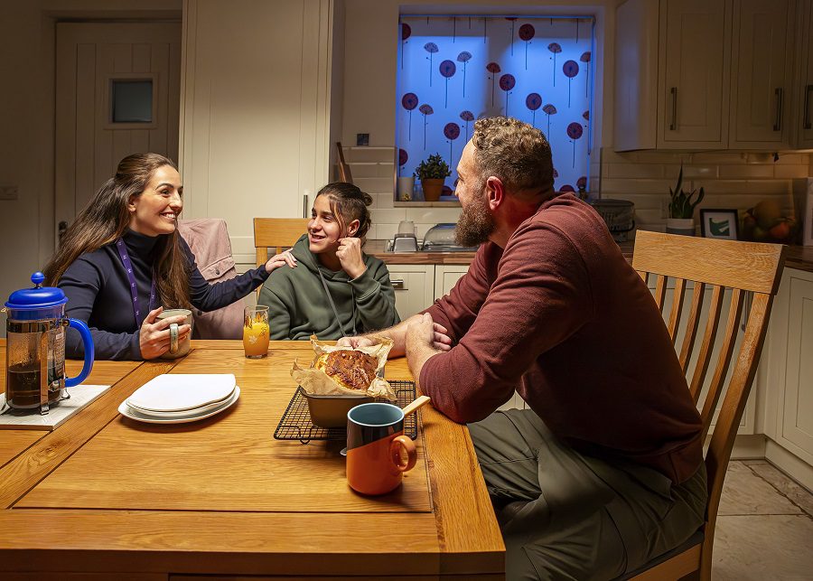 Female social worker, teenage boy and man sat at a kitchen table